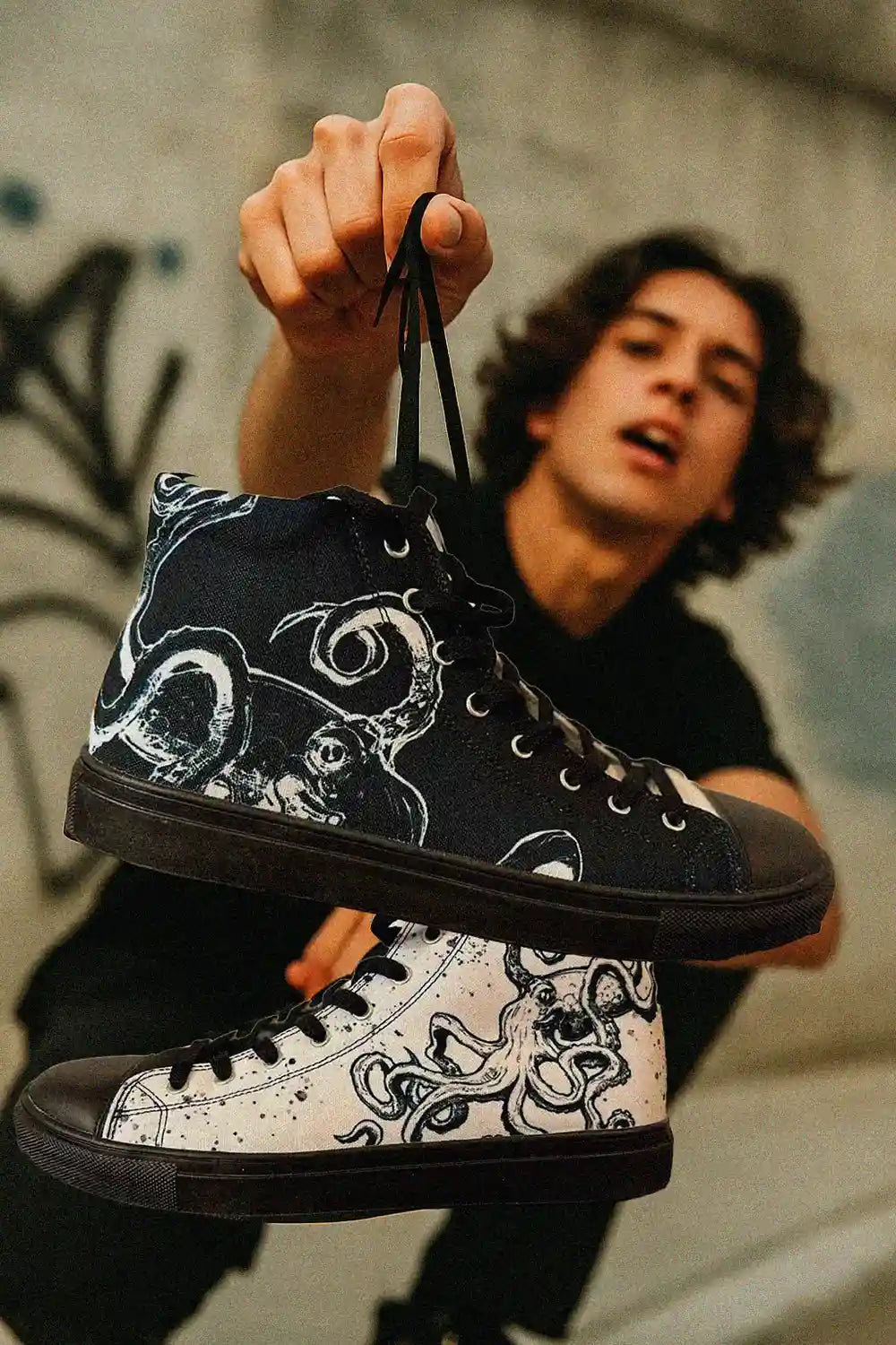 Person holding up a pair of black and white sneakers with intricate designs.