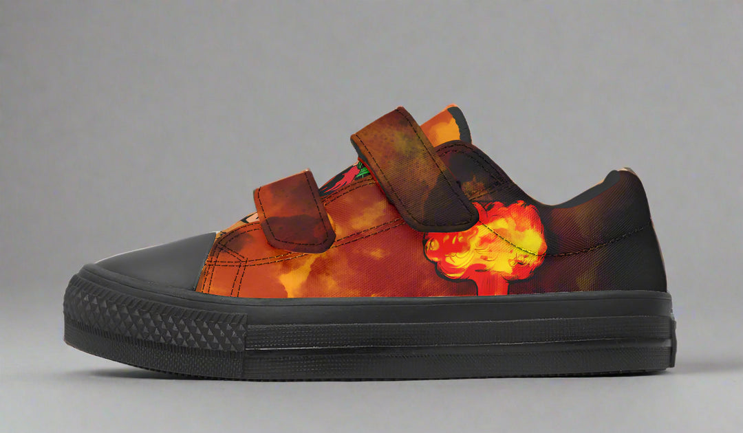 Kids’ low-top sneaker featuring a bright orange-yellow explosion graphic on the outer side of the left shoe. The red-orange smoke blends across the canvas upper, with dual velcro straps and black sole for easy wear and bold style. — Bomber Girl design by Sky Titan Media, made for young adventurers with vintage flair and a fearless sense of style.