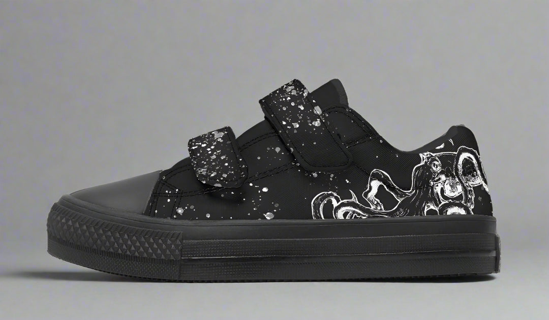 Studio-lit side profile of the Octopus Blackout low-top sneaker in the kids’ edition by Sky Titan Media, highlighting monochrome tentacle artwork, splatter-effect Velcro straps, and a black rubber sole—bringing deep-sea attitude to everyday playwear.