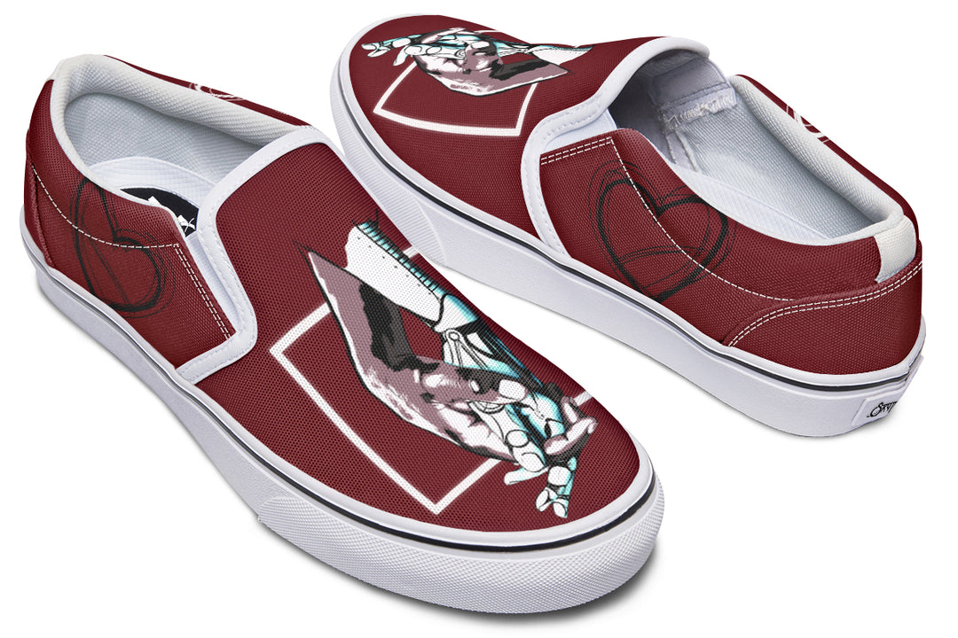 Angled front view of red slip-on sneakers featuring Sky Titan Media’s “July” artwork—two robotic hands meeting inside a diamond frame. Now with a clean white sole and contrast stitching that enhances the shape and layered textures of the upper.