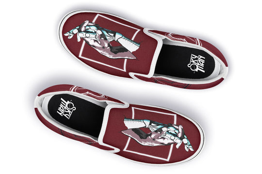 Overhead view of the pair of red “July” slip-ons with white soles. The mirrored hand illustrations remain bold and central, while the enhanced stitching detail elevates both function and design for a cleaner streetwear aesthetic.