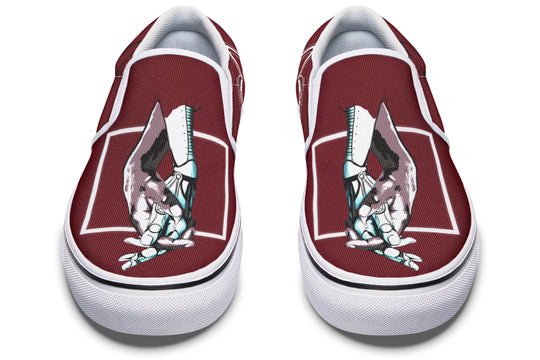Frontal view of the red “July” slip-ons by Sky Titan Media, now featuring bright white soles and visible contrast stitching. The central artwork—robotic hands reaching across dimensions—remains a strong symbol of connection and narrative depth.