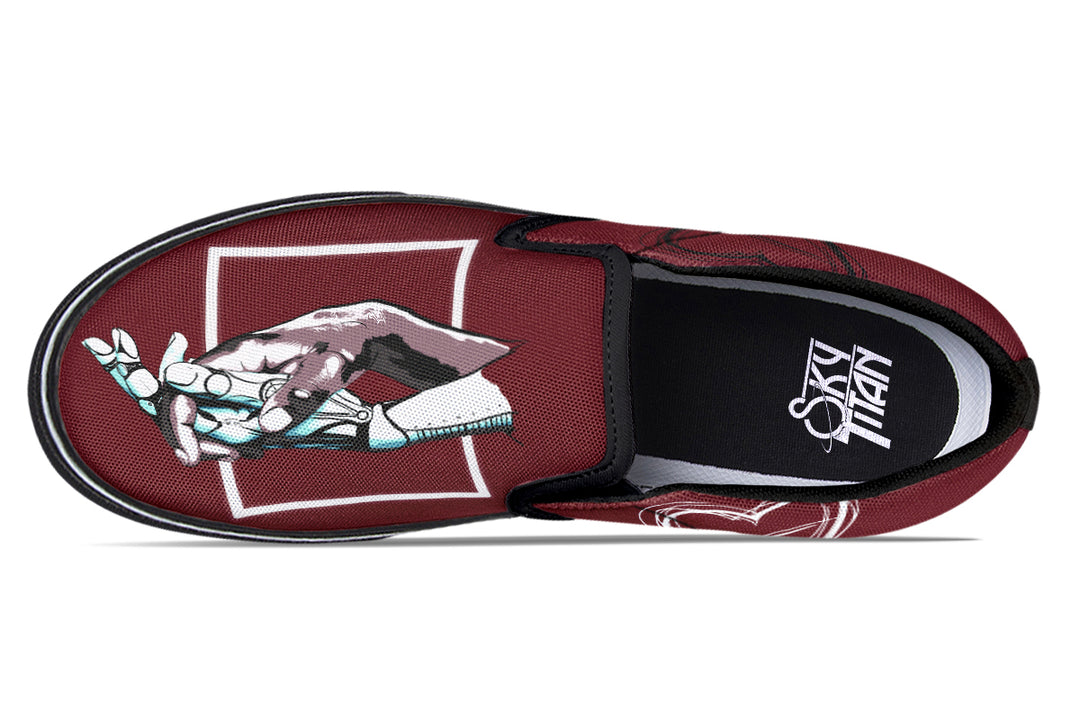 Overhead view of one red slip-on sneaker, displaying the full “July” design artwork—two robotic hands meeting within a sharp geometric box. The black elastic gore and white trim accentuate the central artwork.