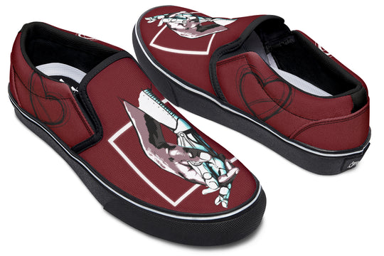 Angled front view of red slip-on sneakers featuring Sky Titan Media’s “July” design—two mechanical hands reaching across a diamond frame. The black midsole and white foxing line contrast with bold upper artwork. Subtle heart line art is visible near the outer ankle, adding an emotional layer to the sci-fi aesthetic.