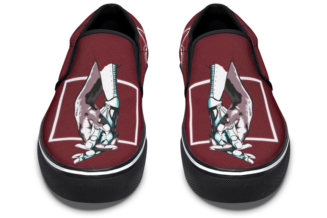 Frontal view of the red slip-on sneakers revealing symmetrical artwork—robotic hands in motion framed by white lines. The elastic inserts and rounded toe cap provide comfort and structure to the sleek silhouette.