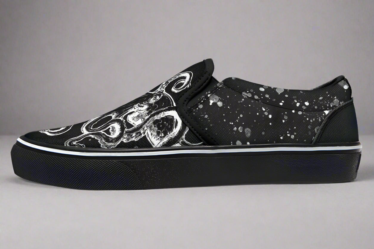 Studio-lit side profile of Sky Titan Media’s Octopus Black Out Edition slip-on sneakers. The detailed white tentacle illustration wraps around the toe box and lateral panel, contrasted by subtle paint-splatter textures. White piping along the sole adds sharp contrast to the shadowy aesthetic.