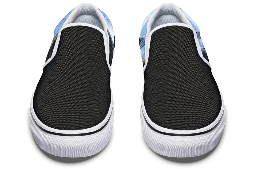Front view of Skybound slip-on sneakers featuring white elastic gores, and white binding. Hints of blue-toned Atlas artwork emerge from the left shoe, while a subtle moon curve with a neon yellow stroke appears on the right. A crisp, mythic silhouette with cosmic energy in every step. — Skybound design by Sky Titan Media, blending mythology-inspired visuals with streetwear rooted in independent music culture.