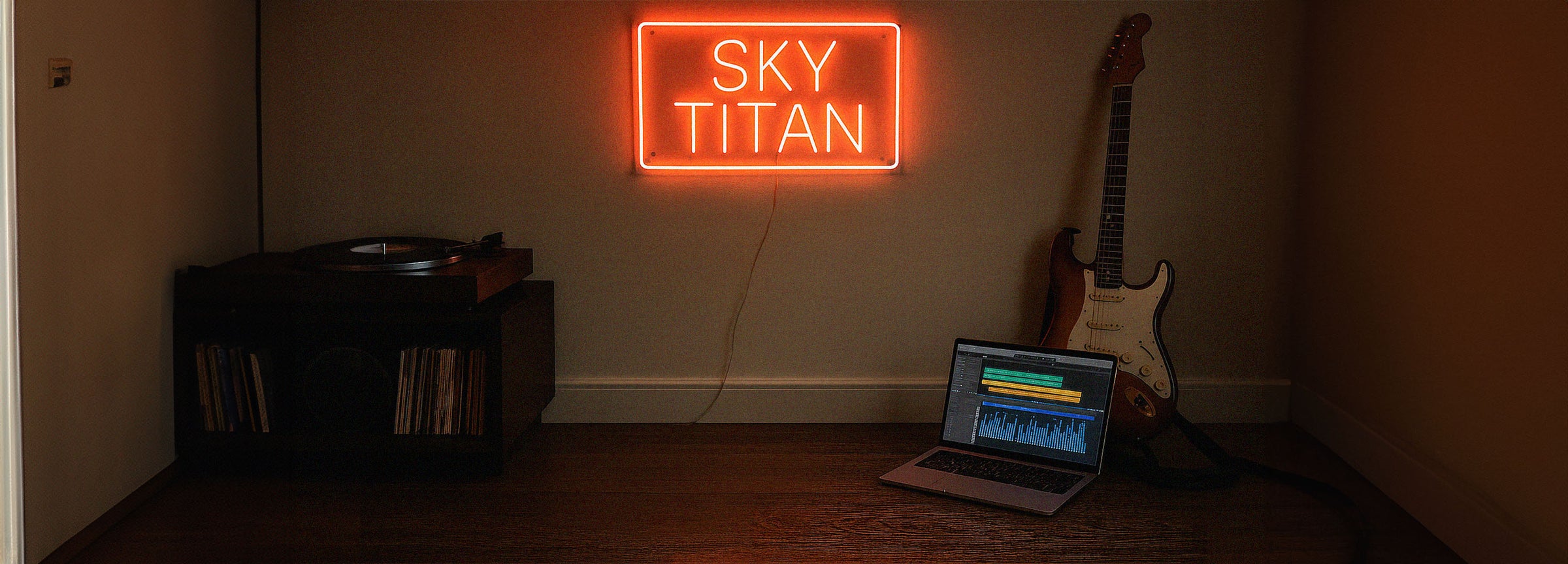 Neon sign reading 'SKY TITAN' above a laptop and guitar in a dimly lit room.