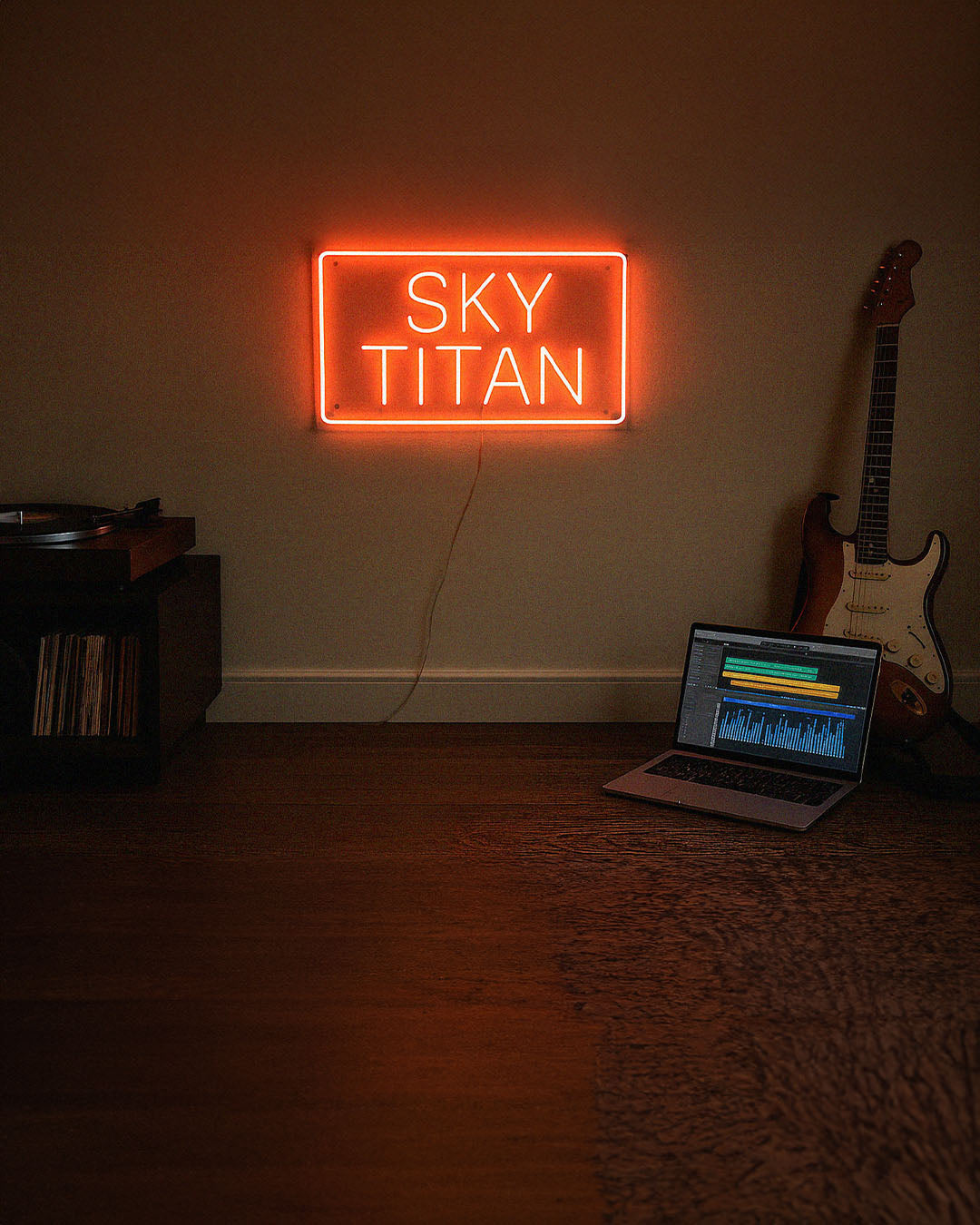 Neon sign reading 'SKY TITAN' in a room with a laptop and guitar.