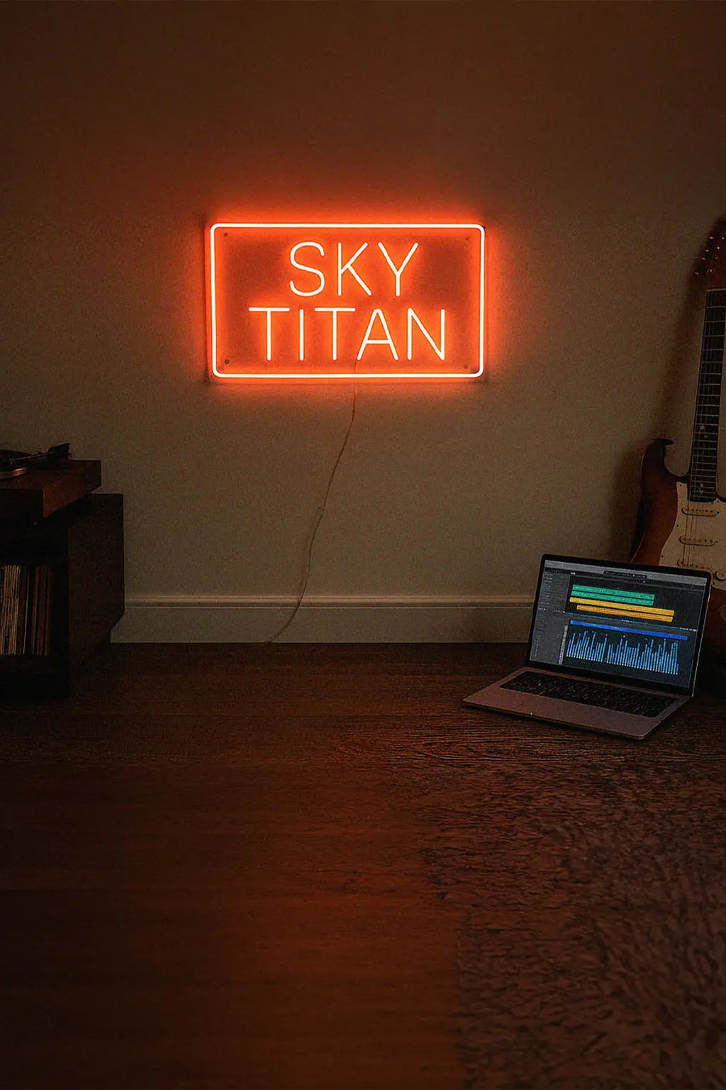 Neon sign reading 'SKY TITAN' in a room with a laptop and guitar.